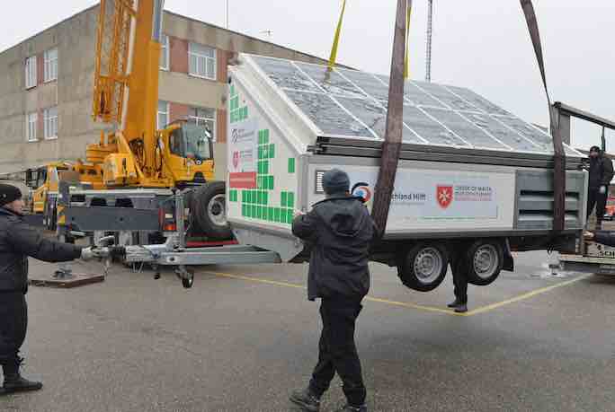 3 men stabilisea large solar panel as it is craned off the boat and onto a lorry for delivery to a hospital