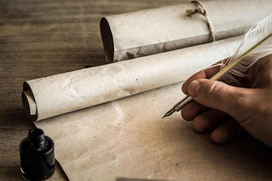 AS hand clutching a quill pen writes on hand made paper