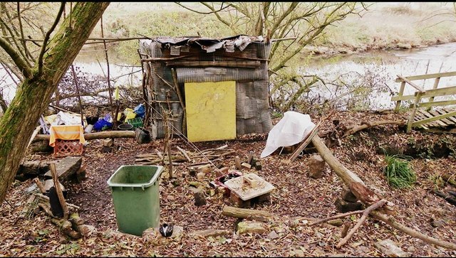 A small compound with a shack, fire, water container