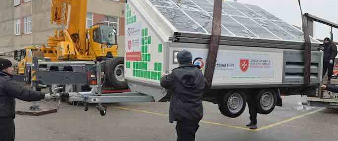 3 men stabilisea large solar panel as it is craned off the boat and onto a lorry for delivery to a hospital