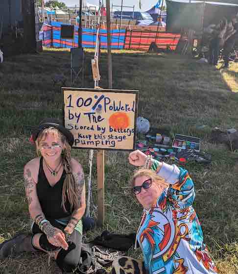 Two festival goers sit in the shade under a sign