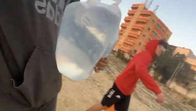 Carrying larg water containers through bombed out streets in Gaza